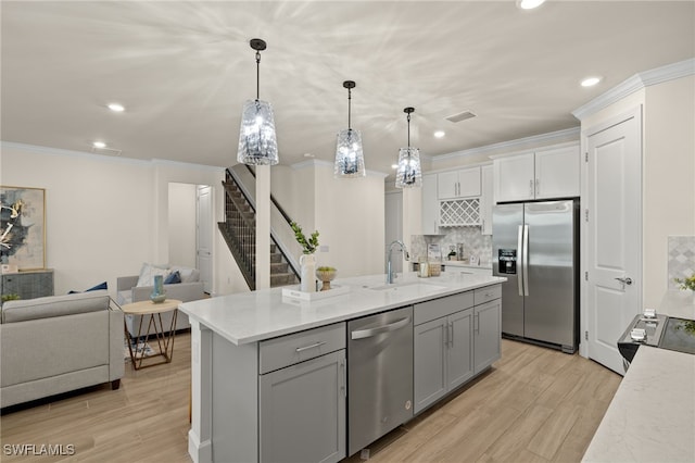 kitchen with gray cabinetry, a center island with sink, hanging light fixtures, light wood-type flooring, and stainless steel appliances