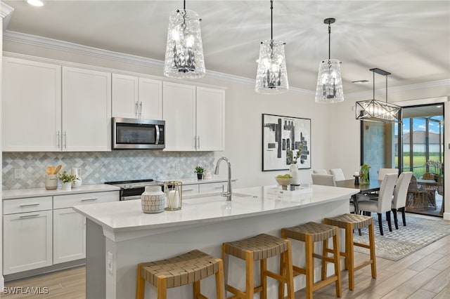 kitchen featuring an island with sink, hanging light fixtures, white cabinets, and stainless steel appliances