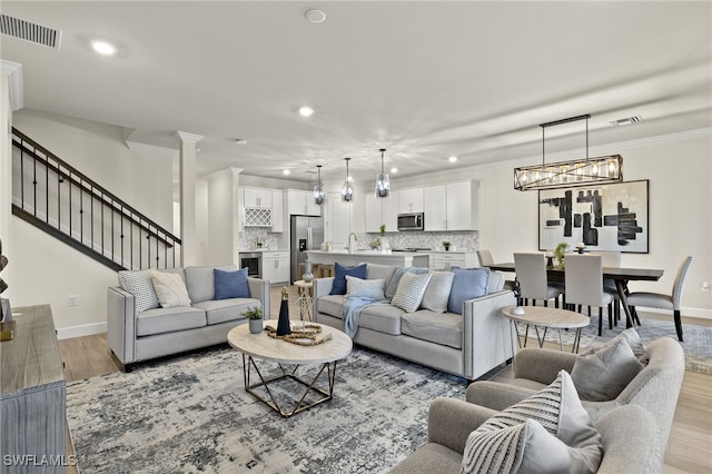 living room featuring sink, light hardwood / wood-style flooring, beverage cooler, and ornamental molding