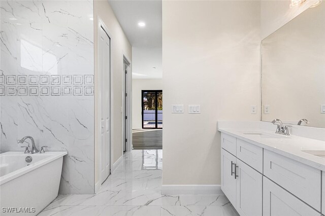 full bath featuring marble finish floor, double vanity, a soaking tub, a sink, and baseboards