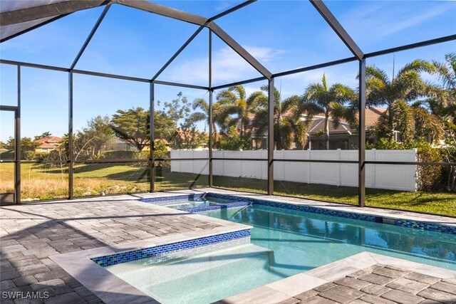 view of swimming pool featuring glass enclosure, fence, a yard, a patio area, and a pool with connected hot tub