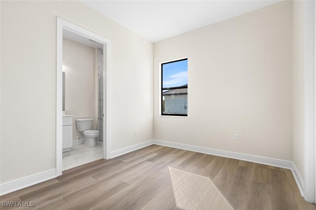 unfurnished bedroom featuring connected bathroom, light wood-style flooring, and baseboards