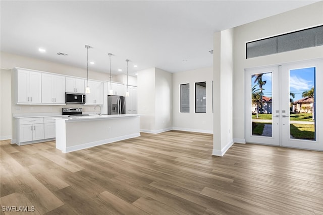 kitchen with stainless steel appliances, white cabinets, hanging light fixtures, light countertops, and a center island with sink