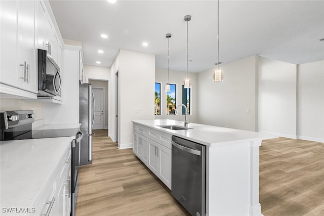 kitchen with a center island with sink, a sink, light countertops, appliances with stainless steel finishes, and light wood-type flooring