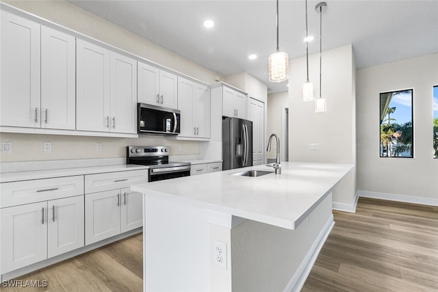 kitchen featuring stainless steel appliances, a sink, white cabinets, light countertops, and an island with sink