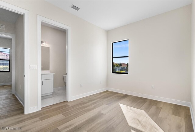 unfurnished bedroom with multiple windows, light wood-type flooring, visible vents, and baseboards