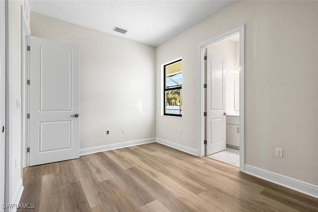 unfurnished bedroom featuring baseboards, visible vents, light wood finished floors, and connected bathroom