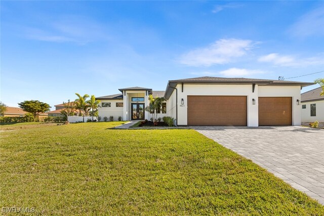 prairie-style house with a garage, decorative driveway, a front lawn, and stucco siding