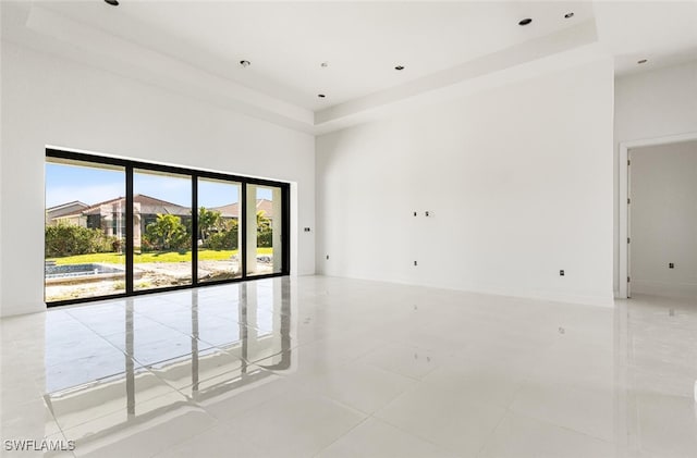 empty room with a raised ceiling, a towering ceiling, and light tile patterned flooring