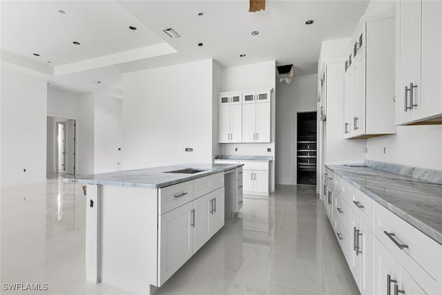 kitchen with a raised ceiling, white cabinetry, a spacious island, and light stone counters