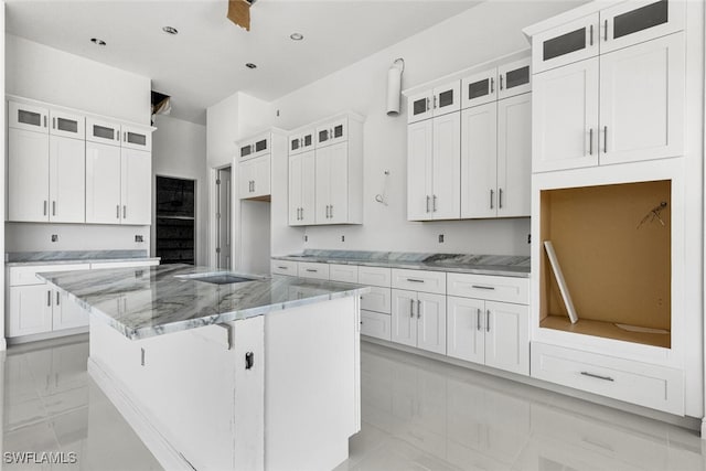 kitchen with white cabinets, ceiling fan, light stone countertops, a kitchen island, and a breakfast bar area