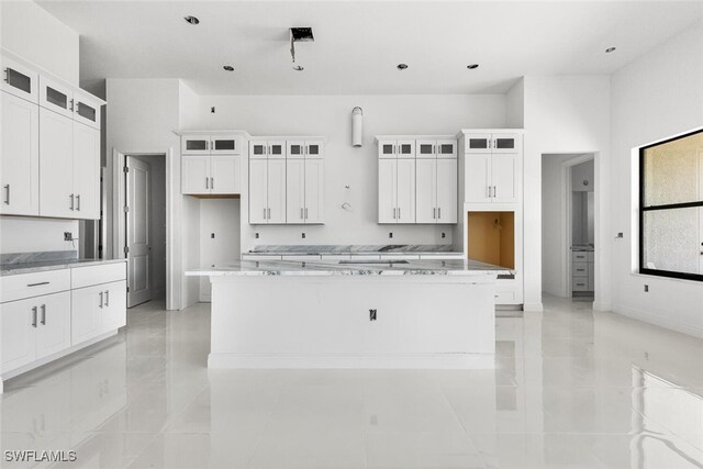 kitchen featuring white cabinets, a towering ceiling, light stone counters, and a large island