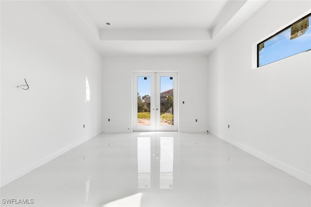 empty room featuring a raised ceiling, light tile patterned floors, and french doors