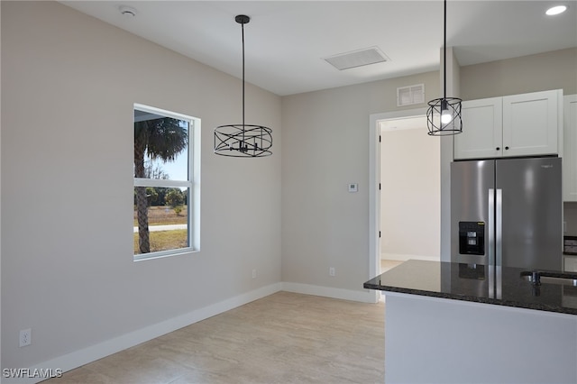 kitchen with baseboards, pendant lighting, dark stone countertops, stainless steel fridge, and white cabinetry