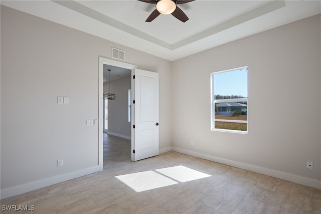 spare room with a tray ceiling, baseboards, visible vents, and ceiling fan