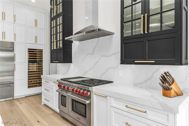 kitchen with high quality appliances, backsplash, exhaust hood, light stone counters, and beverage cooler