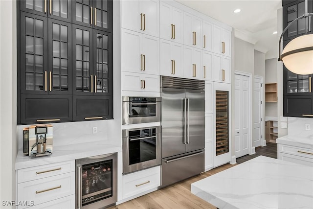 kitchen with wine cooler, built in refrigerator, light wood-type flooring, light stone counters, and white cabinetry