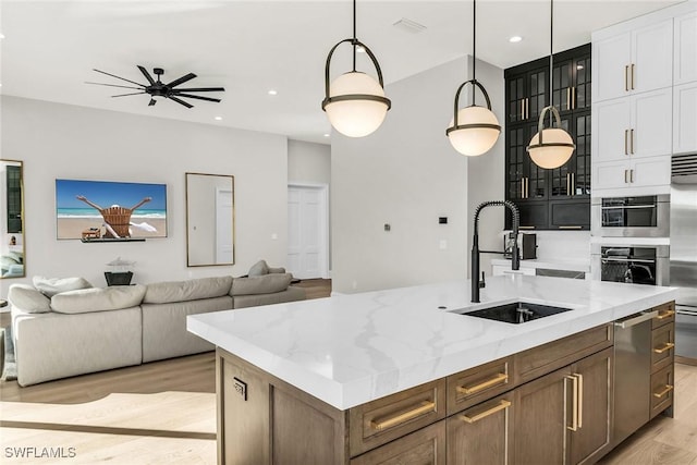 kitchen with light stone countertops, sink, hanging light fixtures, light hardwood / wood-style flooring, and an island with sink