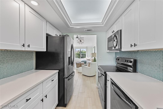 kitchen featuring appliances with stainless steel finishes, white cabinetry, backsplash, a raised ceiling, and crown molding