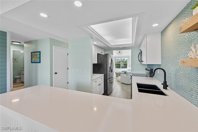 kitchen featuring sink, appliances with stainless steel finishes, kitchen peninsula, a raised ceiling, and white cabinets