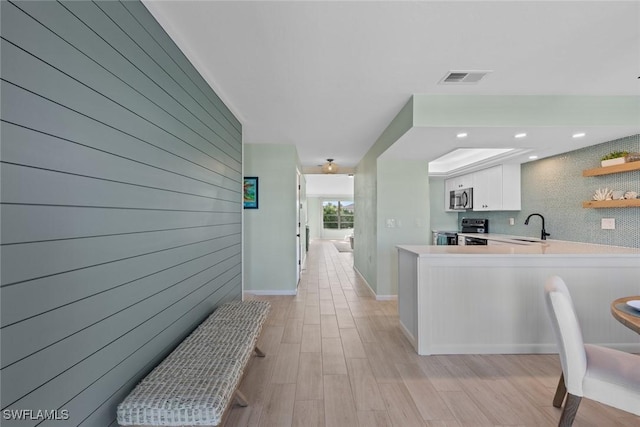 kitchen with sink, appliances with stainless steel finishes, wooden walls, kitchen peninsula, and white cabinets