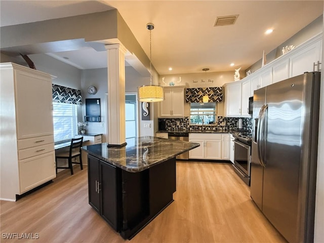 kitchen with dark stone countertops, stainless steel appliances, light hardwood / wood-style floors, decorative light fixtures, and ornate columns