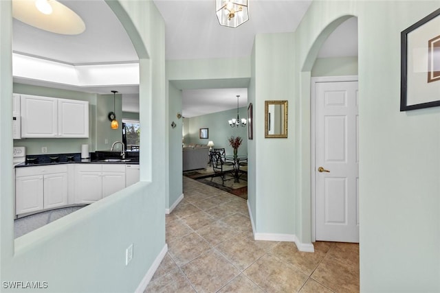 kitchen featuring white cabinets, sink, hanging light fixtures, light tile patterned floors, and a notable chandelier