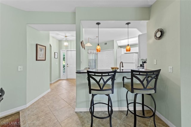 kitchen with kitchen peninsula, a breakfast bar, light tile patterned floors, white fridge, and hanging light fixtures