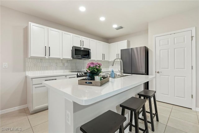 kitchen with backsplash, stainless steel appliances, white cabinetry, and an island with sink