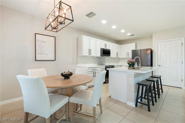 kitchen featuring appliances with stainless steel finishes, tasteful backsplash, a kitchen island with sink, white cabinets, and hanging light fixtures