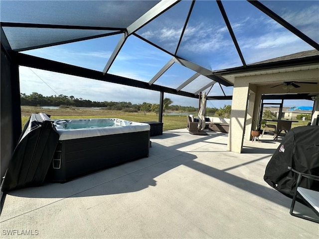 view of patio featuring glass enclosure, a hot tub, and ceiling fan