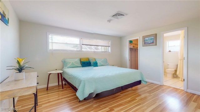 bedroom with light wood-type flooring, ensuite bathroom, a spacious closet, and a closet