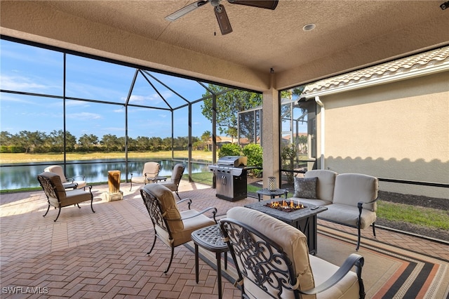 view of patio / terrace with glass enclosure, a water view, ceiling fan, an outdoor living space with a fire pit, and area for grilling