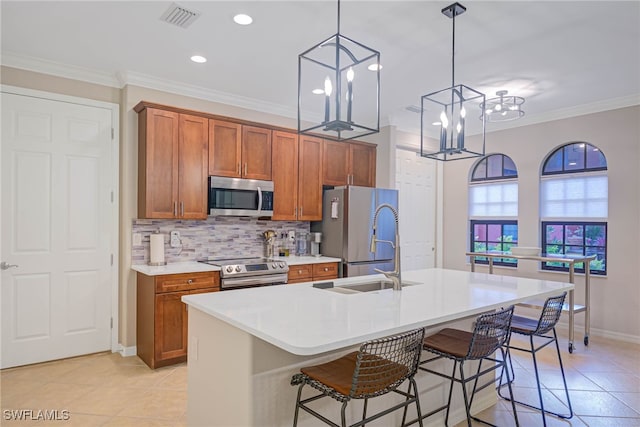 kitchen featuring hanging light fixtures, a breakfast bar area, a kitchen island with sink, appliances with stainless steel finishes, and ornamental molding