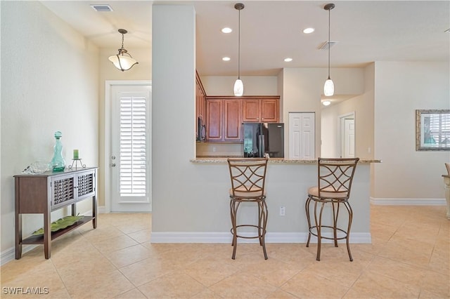 kitchen featuring black refrigerator, a kitchen bar, light stone countertops, light tile patterned floors, and hanging light fixtures