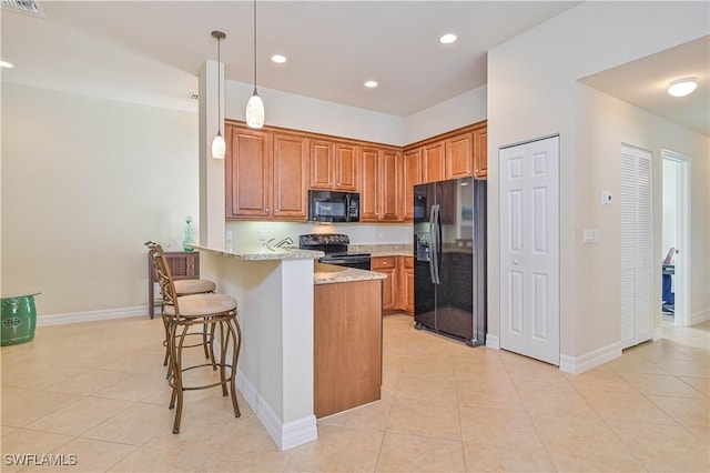 kitchen featuring light stone countertops, kitchen peninsula, decorative light fixtures, a breakfast bar, and black appliances