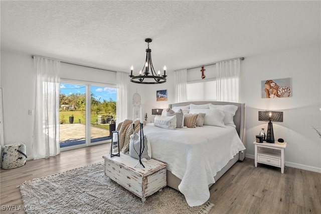 bedroom featuring access to outside, hardwood / wood-style floors, a textured ceiling, and an inviting chandelier