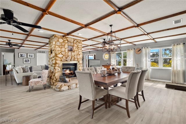 dining area featuring ceiling fan with notable chandelier, light hardwood / wood-style floors, a stone fireplace, and coffered ceiling