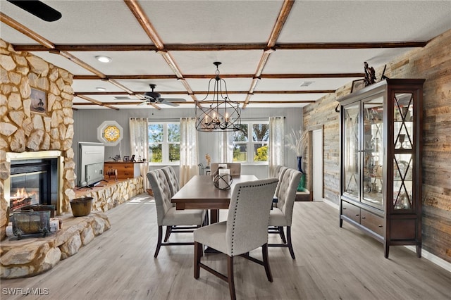 dining space featuring beam ceiling, a fireplace, ceiling fan with notable chandelier, and coffered ceiling