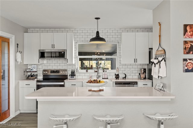 kitchen with white cabinets, decorative backsplash, a kitchen bar, and appliances with stainless steel finishes