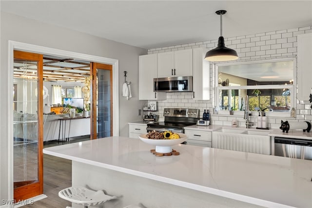 kitchen featuring pendant lighting, decorative backsplash, light stone countertops, white cabinetry, and stainless steel appliances