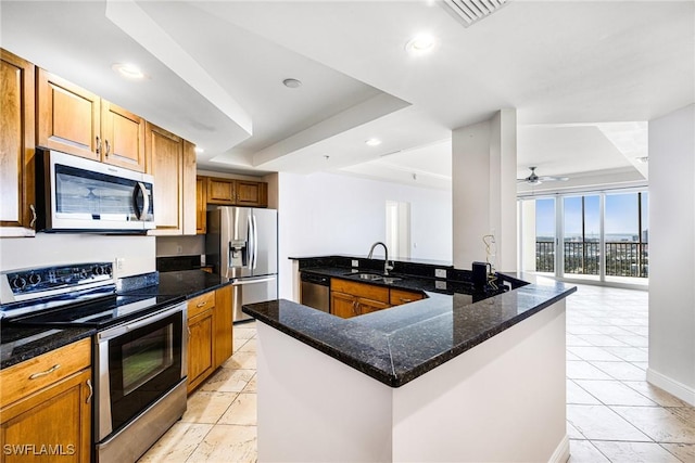 kitchen with dark stone counters, sink, an island with sink, appliances with stainless steel finishes, and a tray ceiling