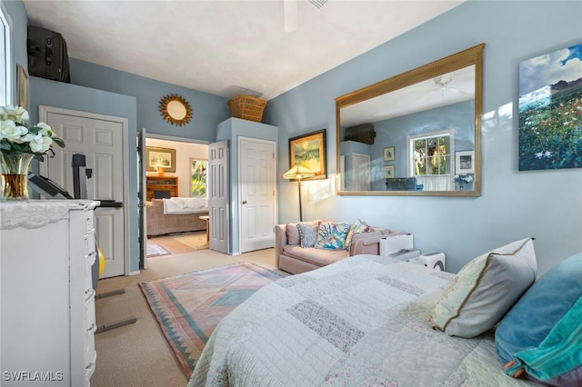 carpeted bedroom featuring ceiling fan, a fireplace, and ensuite bath