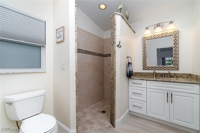 bathroom featuring a tile shower, vanity, toilet, and vaulted ceiling