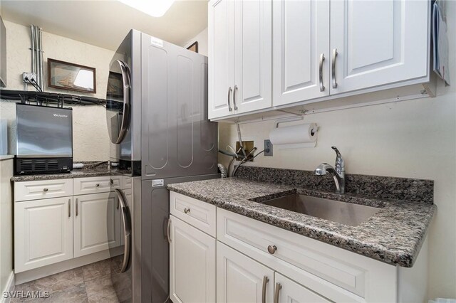 kitchen with sink, white cabinets, dark stone counters, and stacked washer / drying machine