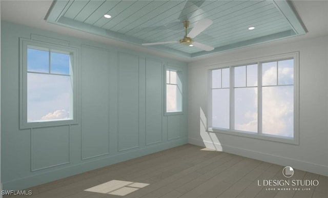 unfurnished room featuring ceiling fan, light wood-type flooring, and a tray ceiling