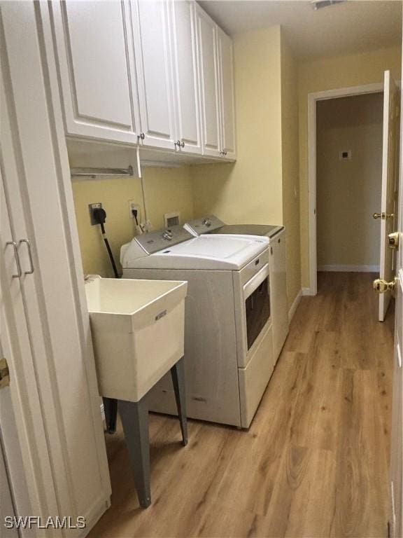 laundry room featuring sink, light hardwood / wood-style flooring, cabinets, and washing machine and clothes dryer