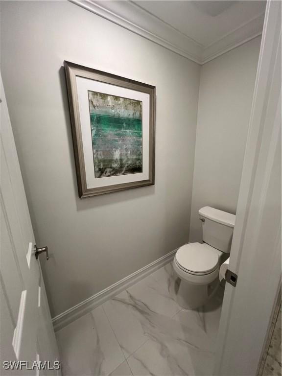 bathroom with marble finish floor, ornamental molding, toilet, and baseboards