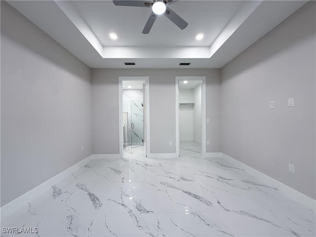 empty room with ceiling fan and a tray ceiling