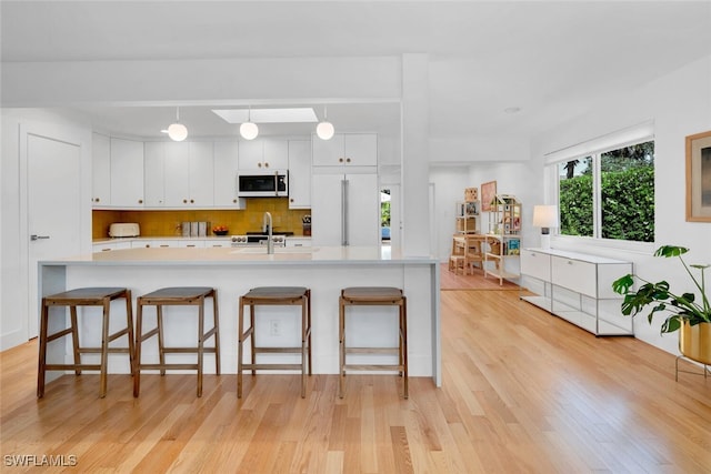 kitchen with a breakfast bar, white appliances, hanging light fixtures, light hardwood / wood-style flooring, and white cabinetry
